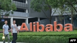 Cette photo d'archive prise le 27 mai 2022 montre des membres du personnel passant devant le logo du géant chinois du commerce électronique Alibaba à son siège social à Hangzhou, dans la province orientale du Zhejiang, en Chine.