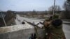 Un militaire ukrainien regarde à travers des jumelles vers la ville de Stoyanka à un point de contrôle avant le dernier pont sur la route qui relie Stoyanka à Kiev, le 6 mars 2022.