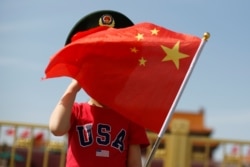 一名站在北京天安門廣場的小男孩身穿美國T卹手拿中國國旗。（2019年5月7日）
