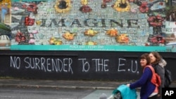 Orang orang berjalan melewati grafiti yang bertuliskan dukungan terhadap gerakan Brexit
di sebuah jalan di bagian barat Belfast, Irlandia Utara, pada 14 Oktober 2019. (Foto: Associated Press)